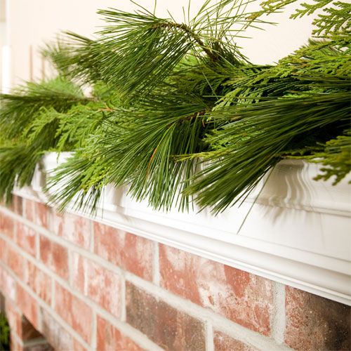 long needle pine boughs draped over a white fireplace mantel above a red brick wall.