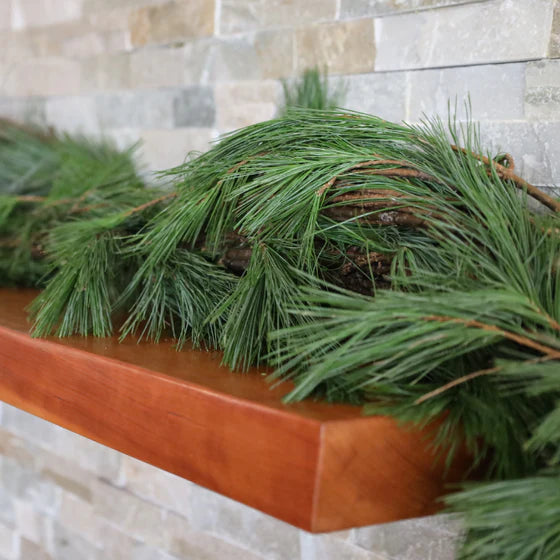 Green pineboughs garland on a wooden mantel against a stone wall.